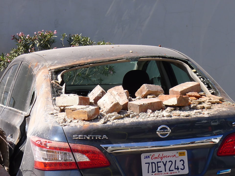 Backsteine und Staub bedecken ein schwer beschädigtes Auto