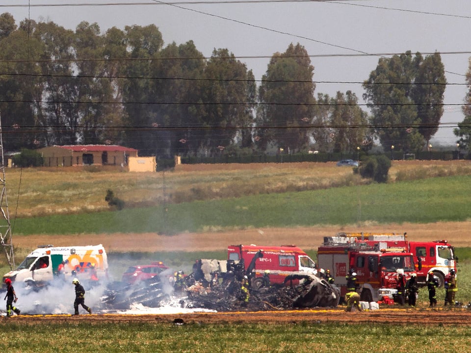 Trümmer eines Flugzeugs auf einem Feld, daneben Feuerwehrautos. 