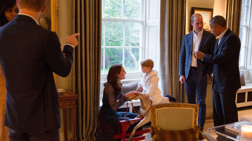 Prinz George auf seinem Schaukelpferd. Mama Kate kniet vor ihm. Harry uns Michelle ubterhalten sich wärend William und Barak zusammen reden. 