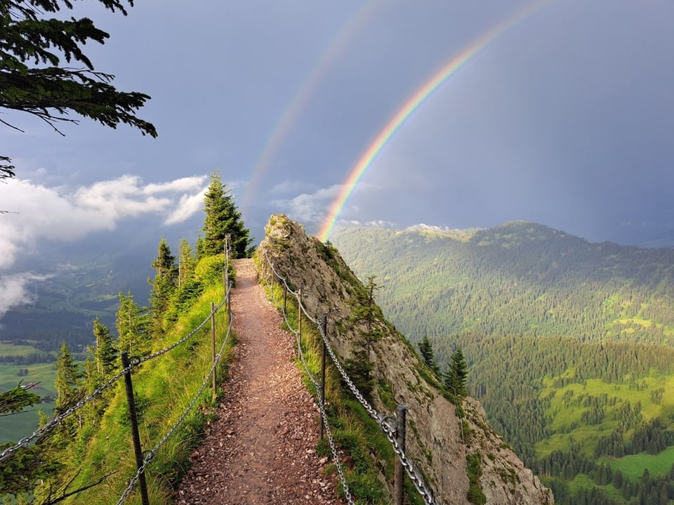 Wanderweg über steile Krete mit doppeltem Regenbogen auf der rechten Seite.
