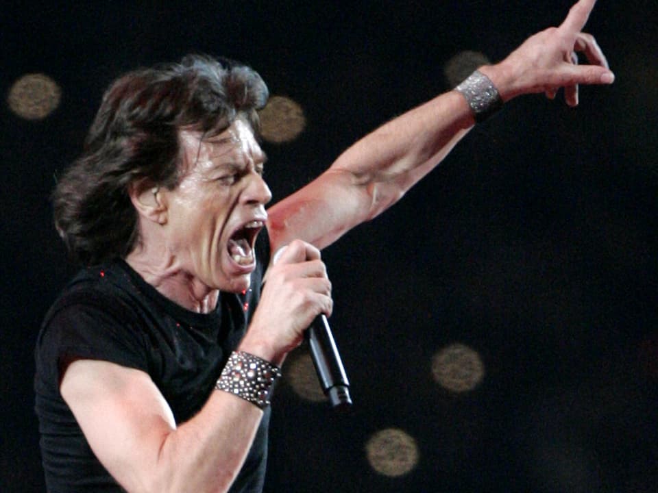 Mick Jagger scherit verschwitzt auf der Bühne in sein Mikrofon.
