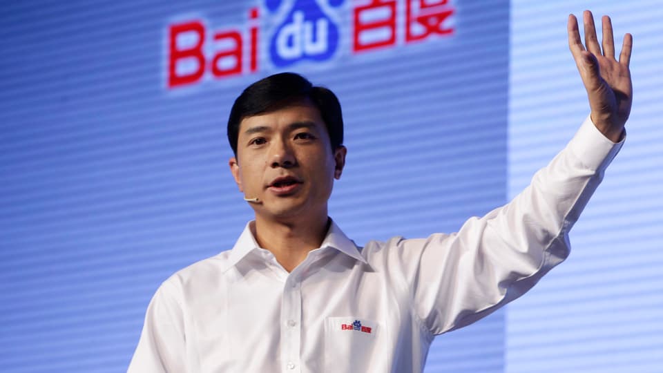Der Baidu-Mitbegründer Robin Li steht vor einem Logo des Unternehmens.