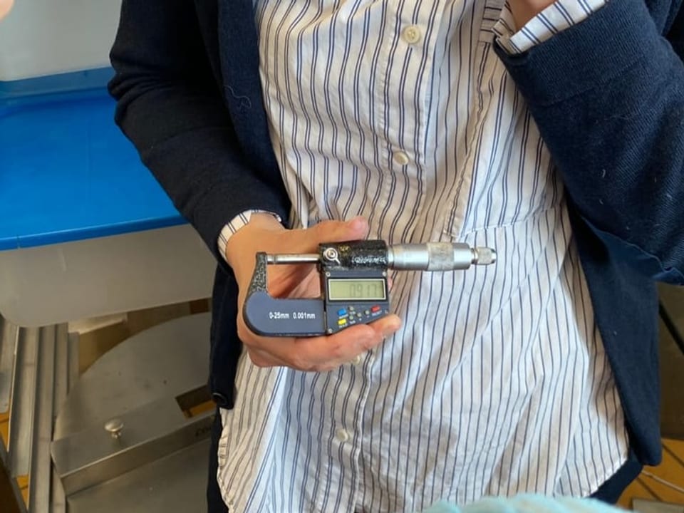Schritt 3: Qualitätskontrolle Im Zentrum steht eine Hand, die eine Art Klemme hält. Die Hand gehört zu Laura.