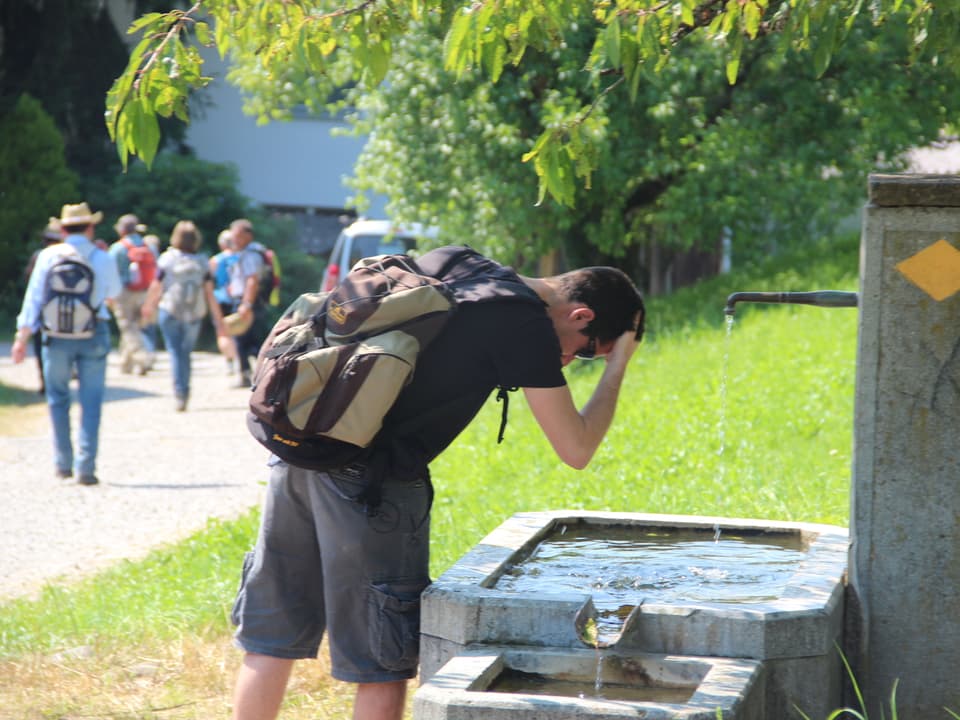 Mann netzt sich den Kopf mit kühlem Wasser aus dem Dorfbrunnen.