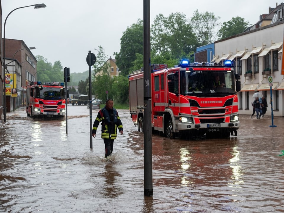 Feuerwehrfahrzeuge und Feuerwehrmann bei Hochwasser in einer Stadt.