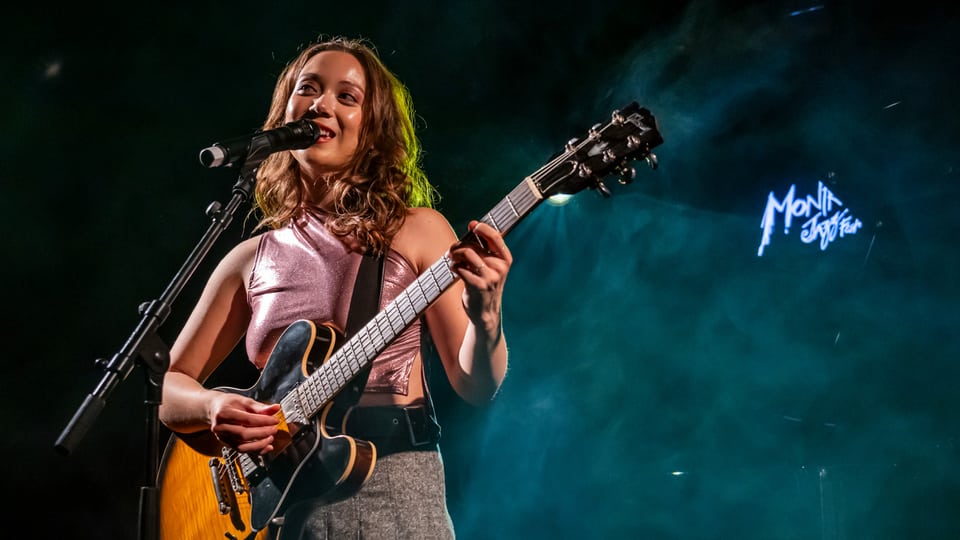 Junge Frau singt auf einer Bühne, hinter ihr blauer Nebel und eine Neon-Schrift des Montreux Jazzfestival.
