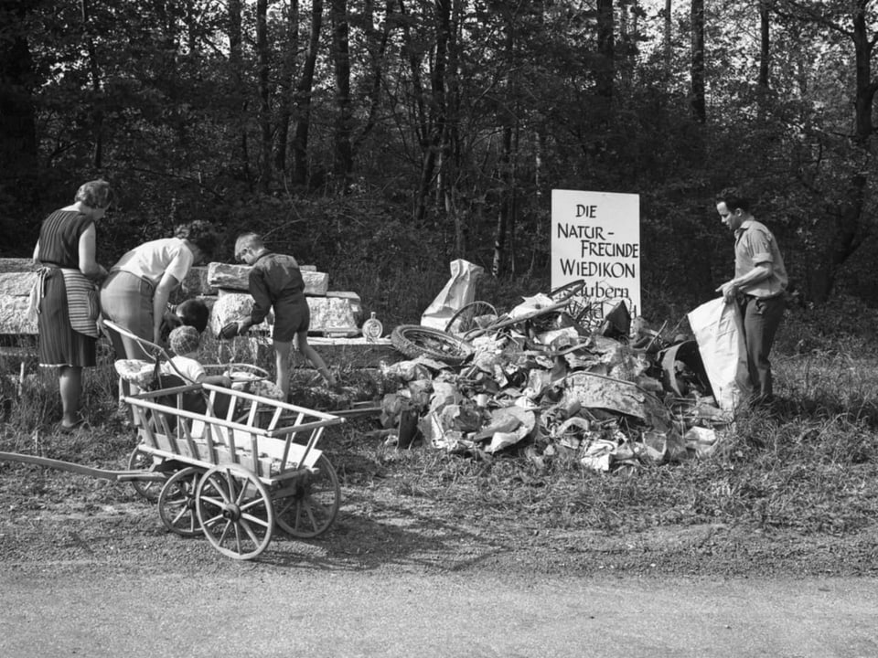 Ein Haufen mit Abfall, dazwischen arbeitende Freiwillige, im Vordergrund Leiterwagen