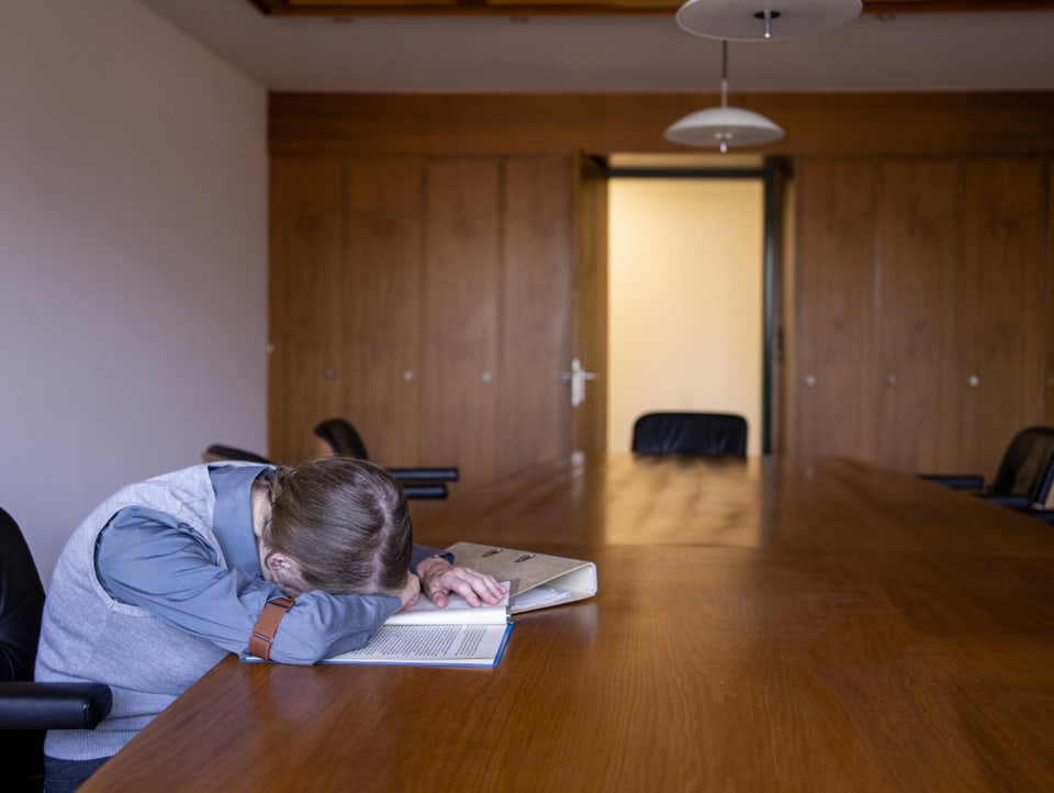 Ein Mann in einem Sitzungszimmer, eingeschlafen über einem aufgeschlagenen Dossier.