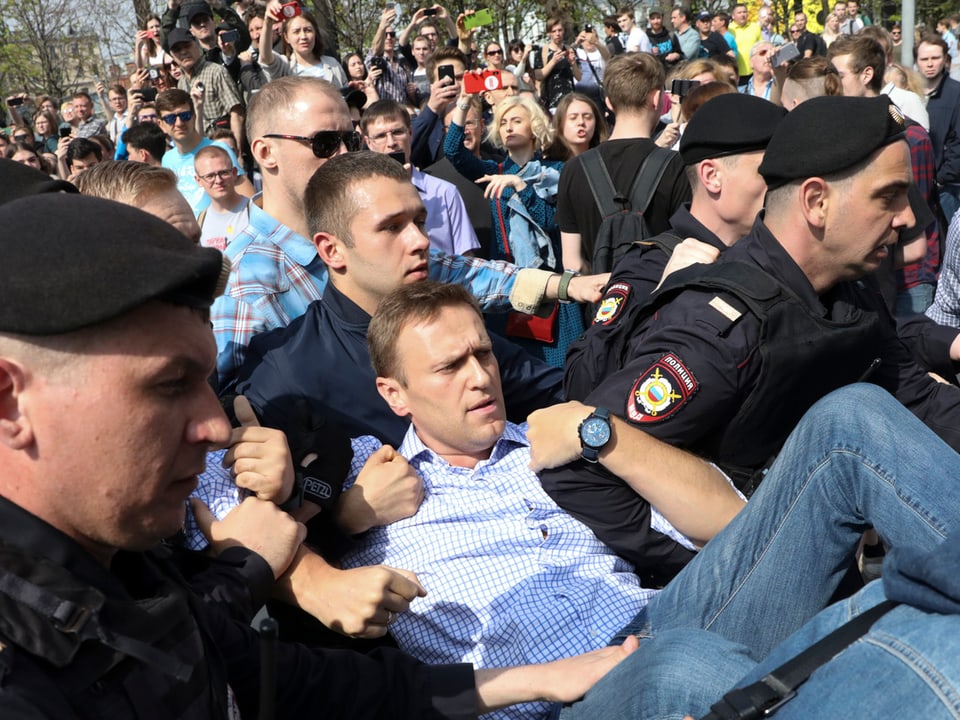 Nawalny wird von Polizisten weggetragen.