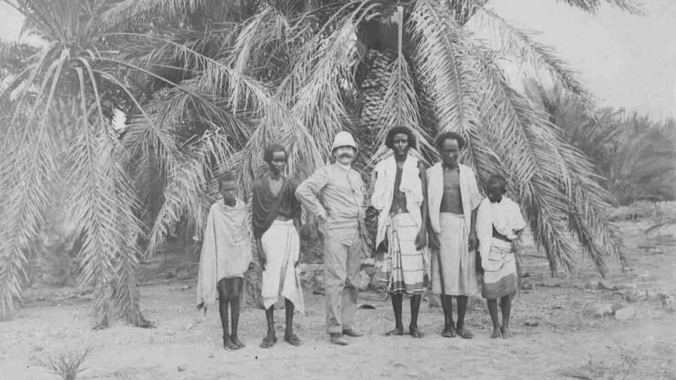 Historische Aufnahme von Victor Solioz. Männer stehen vor Palmen.