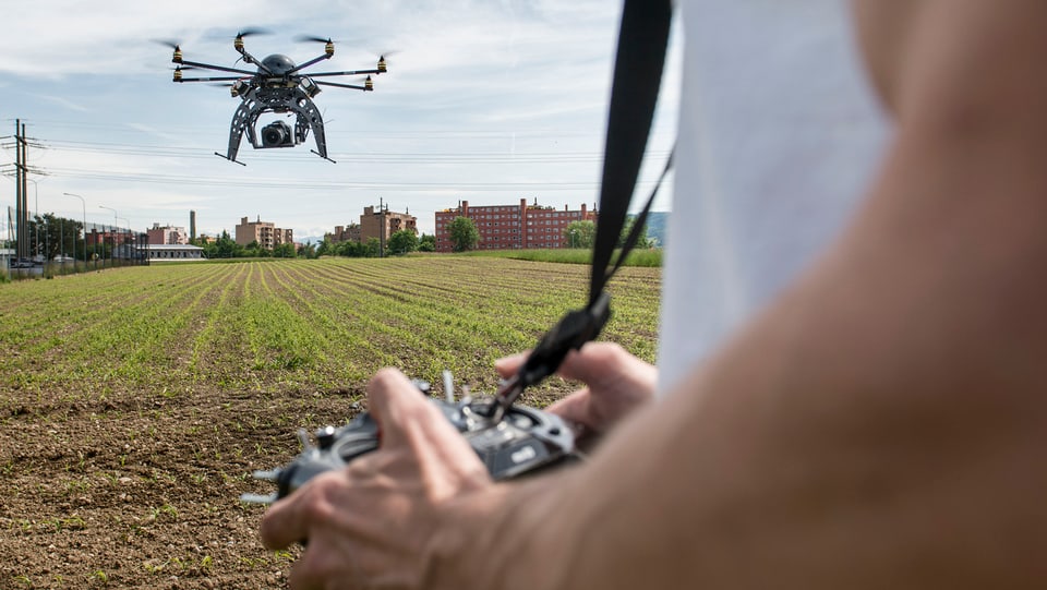 Ein Mann steuert eine Drohne, die eine Spiegelreflexkamera tragen kann, über freiem Feld.