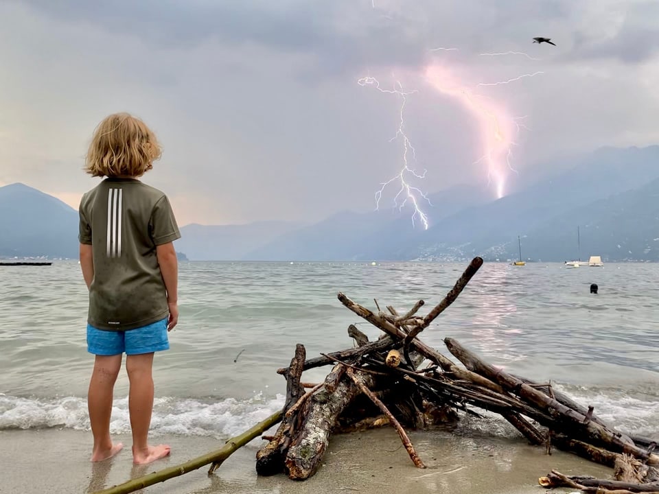 Kind steht am Ufer und schaut zu einem Gewitter