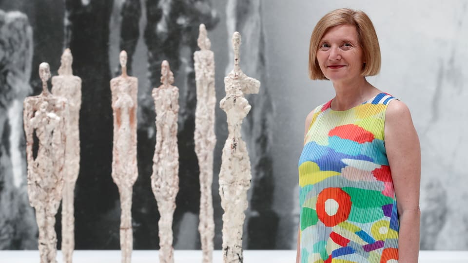 Eine Frau steht vor vier Giacometti-Skulpturen.