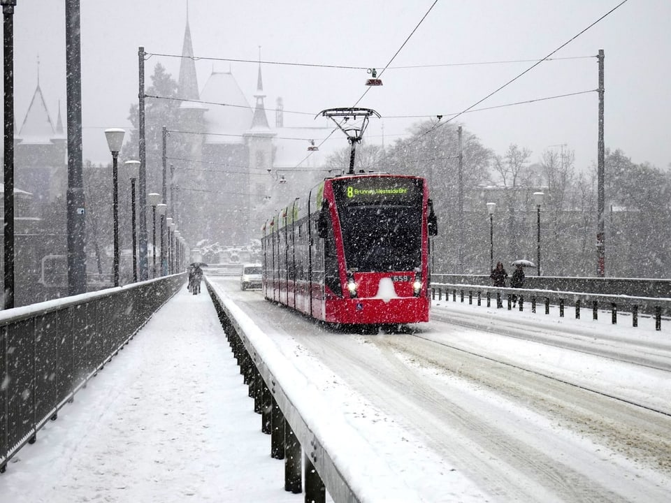 Ein rotes Tram auf einer verschneiten Brücke in Bern.