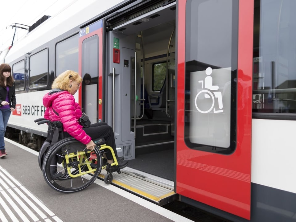 Eine Frau fährt mit einem Rollstuhl in einen Zug hinein.