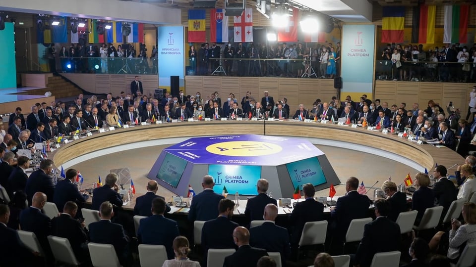 Menschen, vor allem Männer, sitzen um einen riesigen Tisch am Krim-Gipfel.