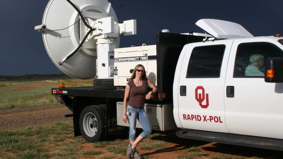 Eine Frau steht vor einem grossen Pickup-Truck, darauf ist eine Satellitenschüssel befestigt.