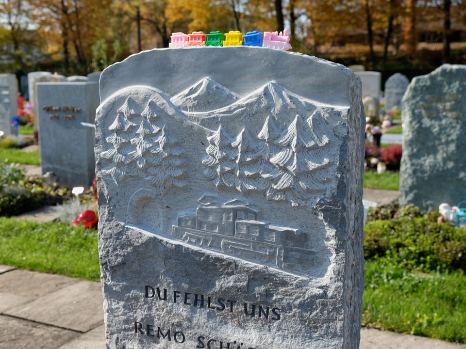 Ein Grabstein mit eingraviertem Zug, auf den ein Plastikzug abgestellt wurde.