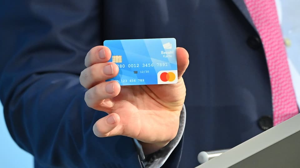 The person holds a blue payment card to the camera