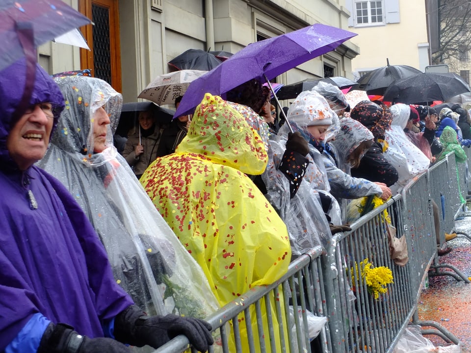 Zuschauer mit Schirm und Regenschutz