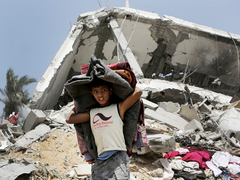 Palästinensischer Junge trägt Matratzen aus zerstörtem Haus