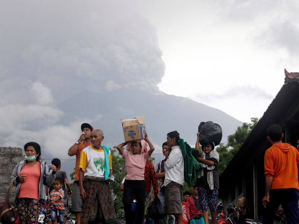 Aschewolke über dem Vulkan Agung. Im Vordergrund fliehende Menschen.