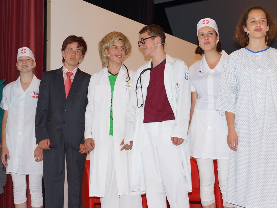 Mit Arztkitteln verkleidete Schülerinnen und Schüler auf der Theaterbühne.