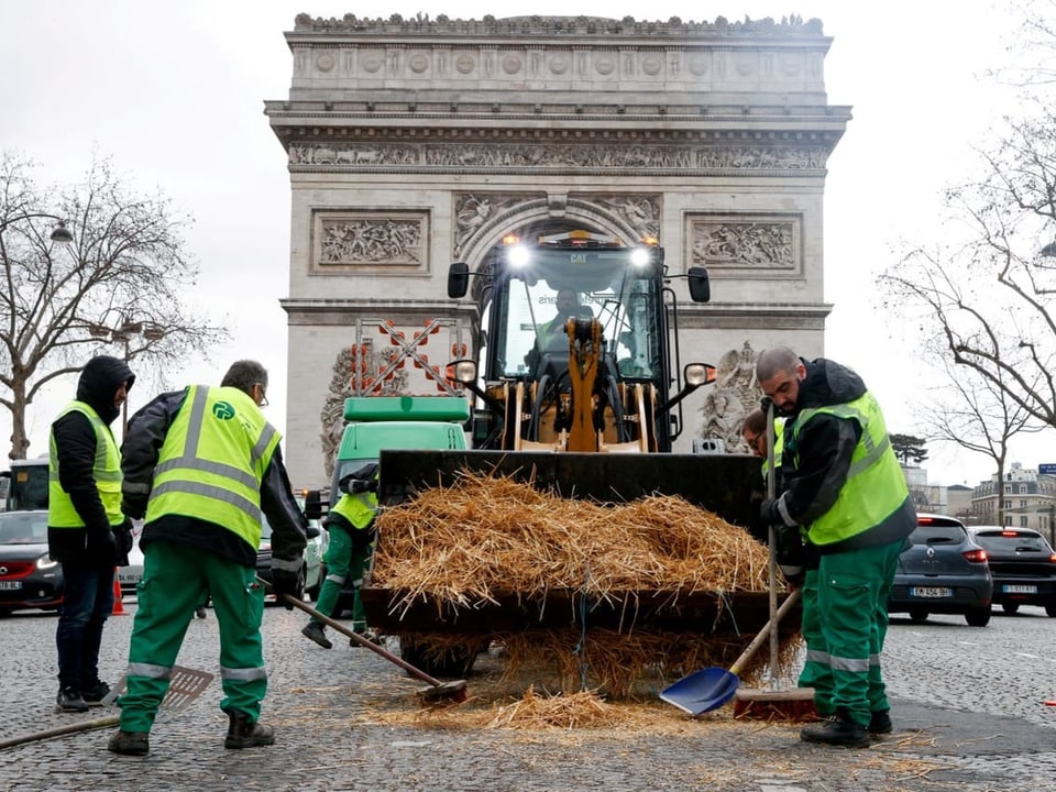 Ein Traktor steht vor dem Arc de Triomphe in Paris. Stroh liegt auf dem Boden und in der Schaufel des Traktors.