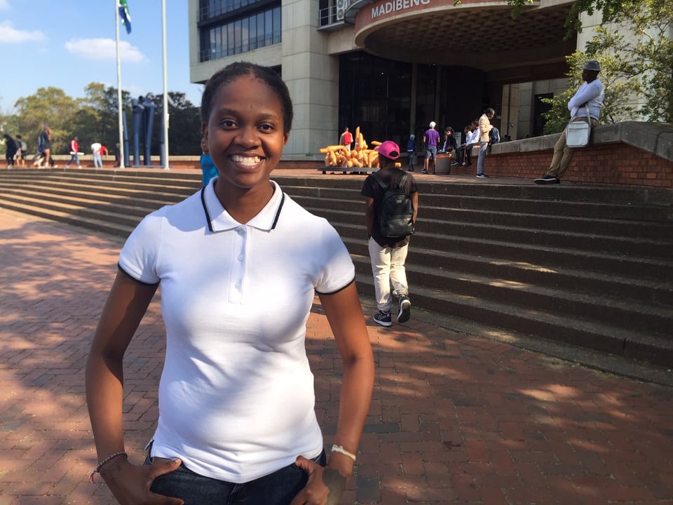 Studentin der Erziehungswissenschaften in weissem T-Shirt steht vor der Universität Johannesburg