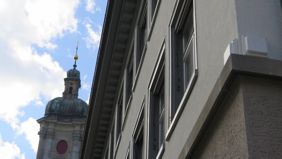 Zwei weisse Kästchen an einer Hausmauer, im Hintergrund der St. Galler Dom.