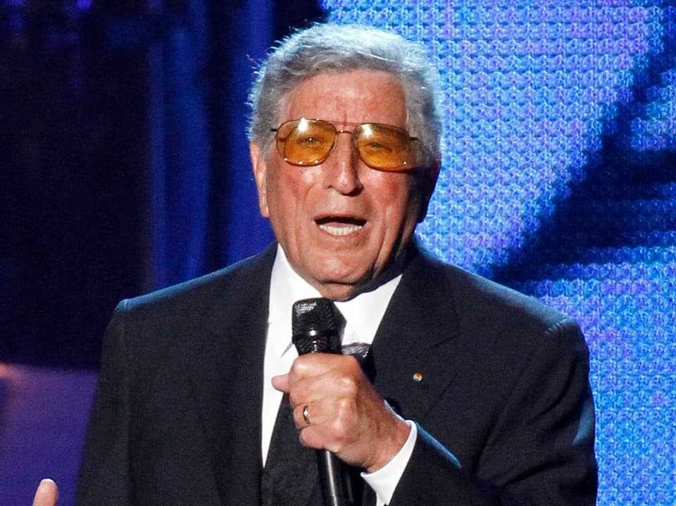 Mann mit grauen Haaren, Brille und Mikrofon steht auf der Bühne und singt.