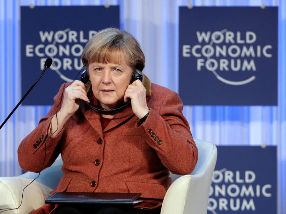 Angela Merkel hält sich die Kopfhörer über die Ohren