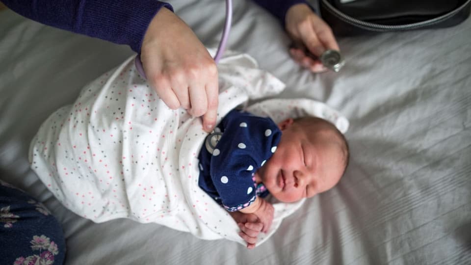 Ein schlafendes Baby, dem der Arzt die Herztönte abhört.