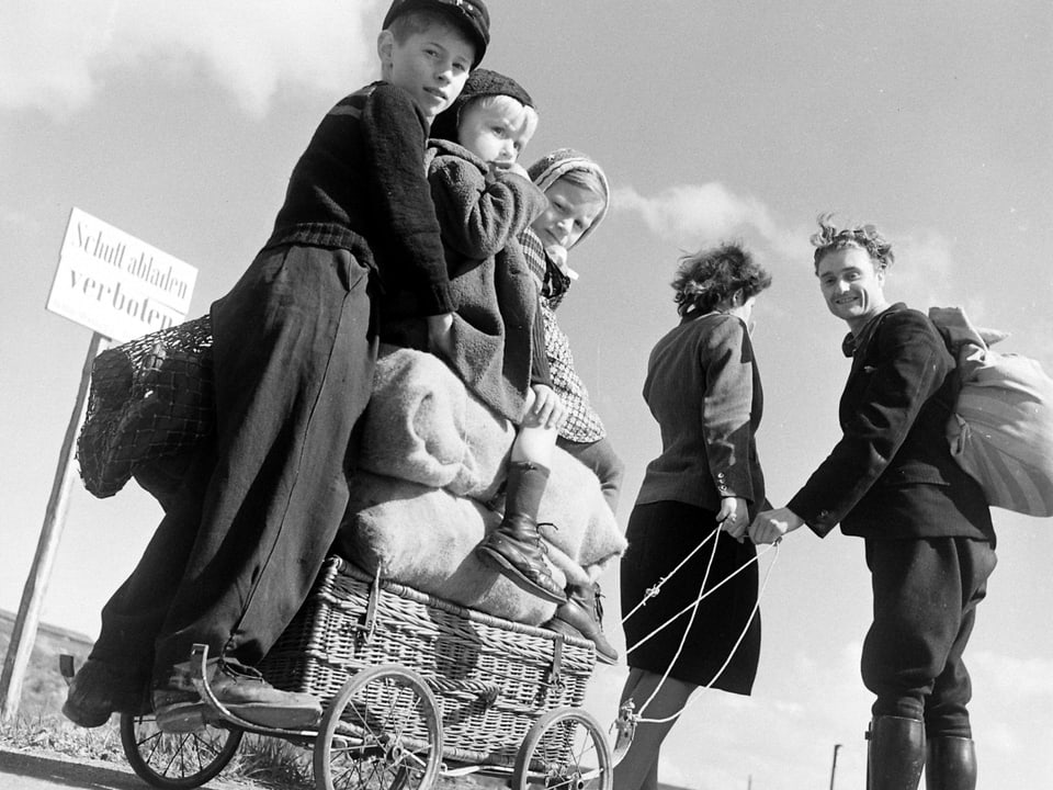 Drei Kinder und Proviant auf einem Leiterwagen, gezogen von den Eltern. 