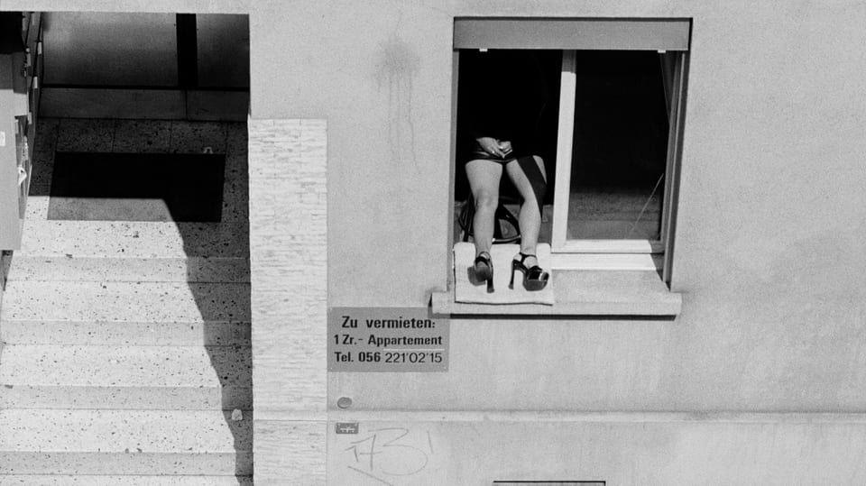 Schwarzweiss-Foto: Prostituierte sitzt am Fenster, nur ihre Beine sind zu sehen.