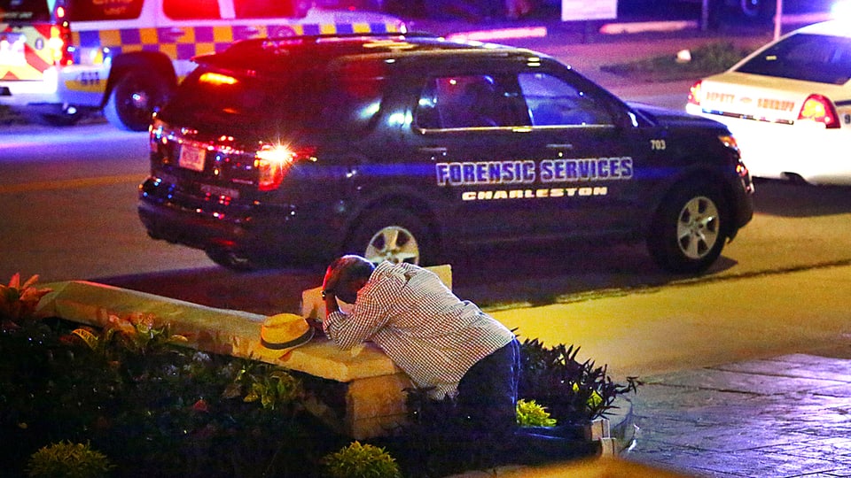 Ein Mann in Charleston im US-Bundesstaat South Carolina kauert im Vordergrund am Boden und hält seinen Kopf. Im Bild Mittelgrund ist ein Polizeifahrzeug bei Nacht zu erkennen.
