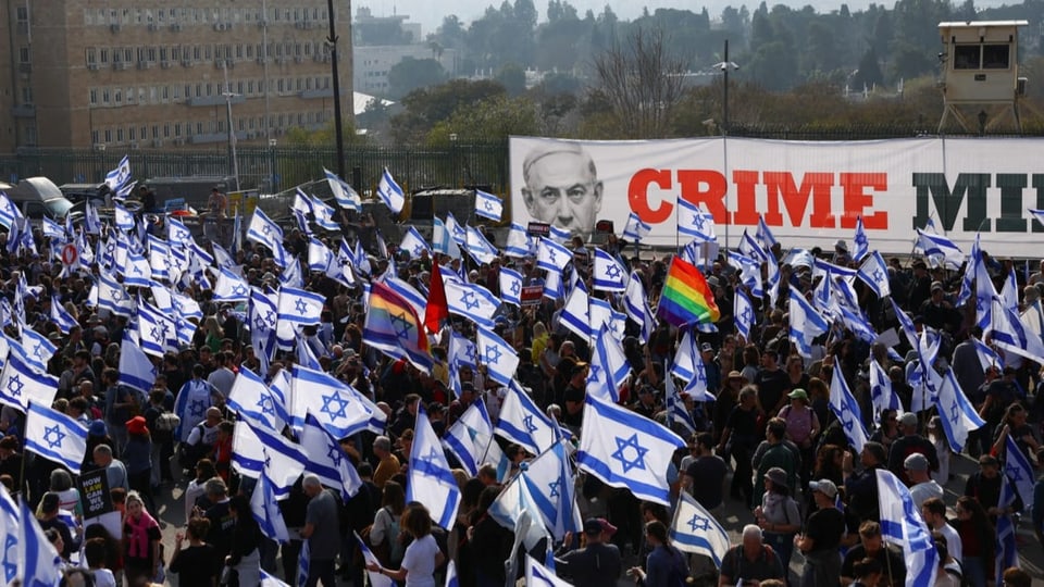 Eine Menschenmenge mit vielen Israel-Flaggen und einem grossen Transparent im Hintergrund mit der Aufschrift «Crime».
