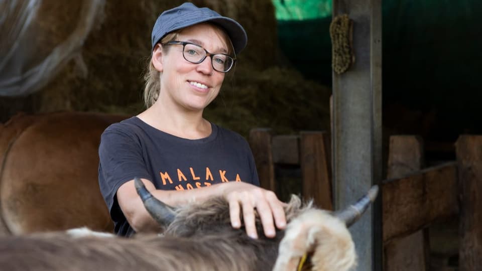 Junge Frau mit Brille und Mütze streichelt eine Kuh.
