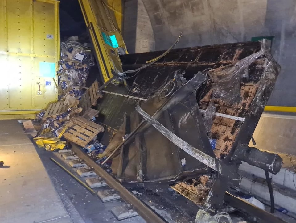 Ein verunfallter Güterwagen liegt auf einem Gleis im Tunnel. Ein Tor im Hintergrund ist zerstört.