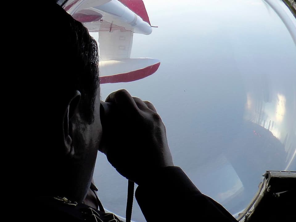 Ein Mann mit Fernglas schaut durch ein Flugzeugfenster.