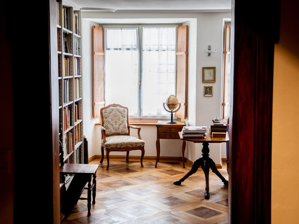 Ein Blick in ein Wohnzimmer mit Parkettboden, Bücherregal, Sessel.