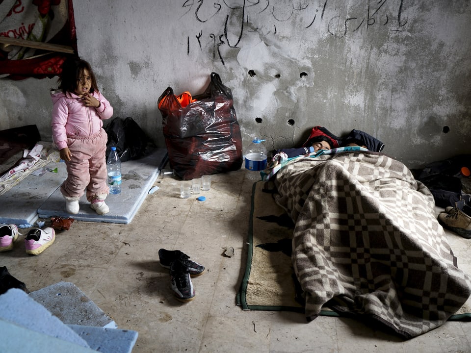 Eine Frau liegt unter Decken in einer Unterbringung auf Chios. Daneben steht ein verschmutztes Kleinkind. (reuters)