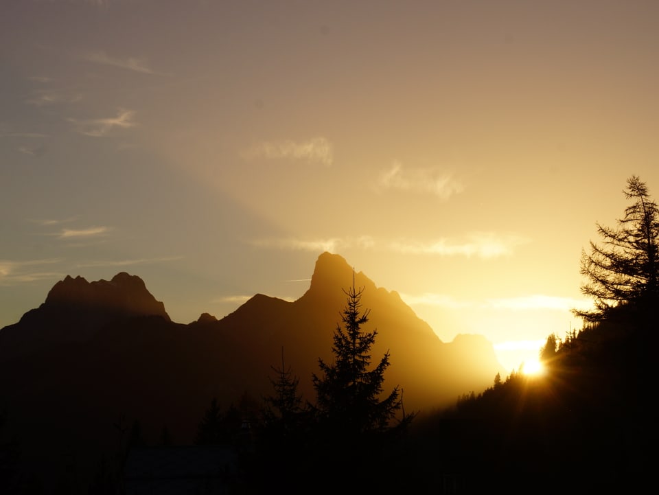 Die Sonne verschwindet hinter einem spitzen Berg.