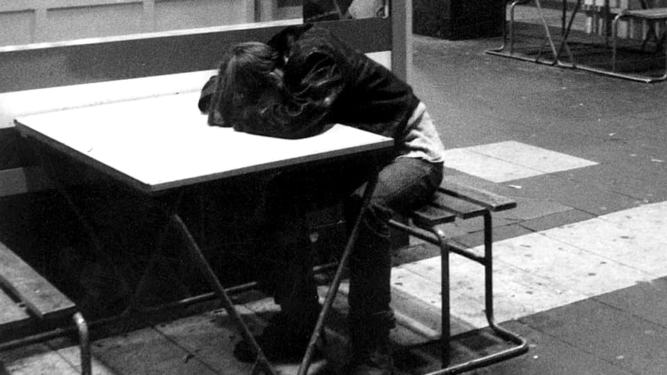 Schwarzweiss-Aufnahme eines Jugendlichen, der betrunken an einem Tisch im Freien schläft.