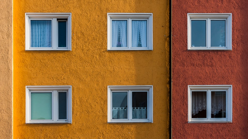 Blick auf eine gelbe Hauswand eines Wohnblocks. Zwei Stockwerke und 6 Fenster sind sichtbar.