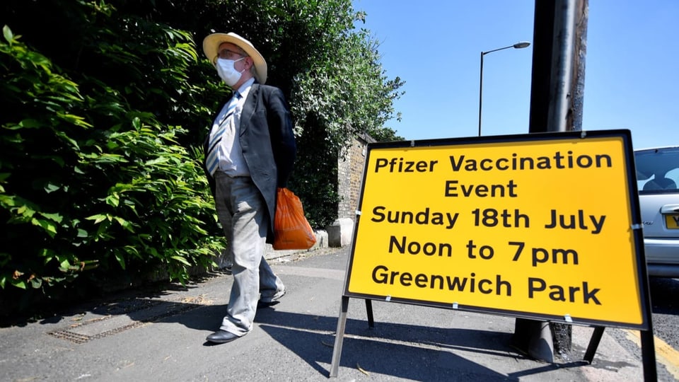 Mann läuft an Schild vorbei, das Impfung in einem Park in London anbietet.