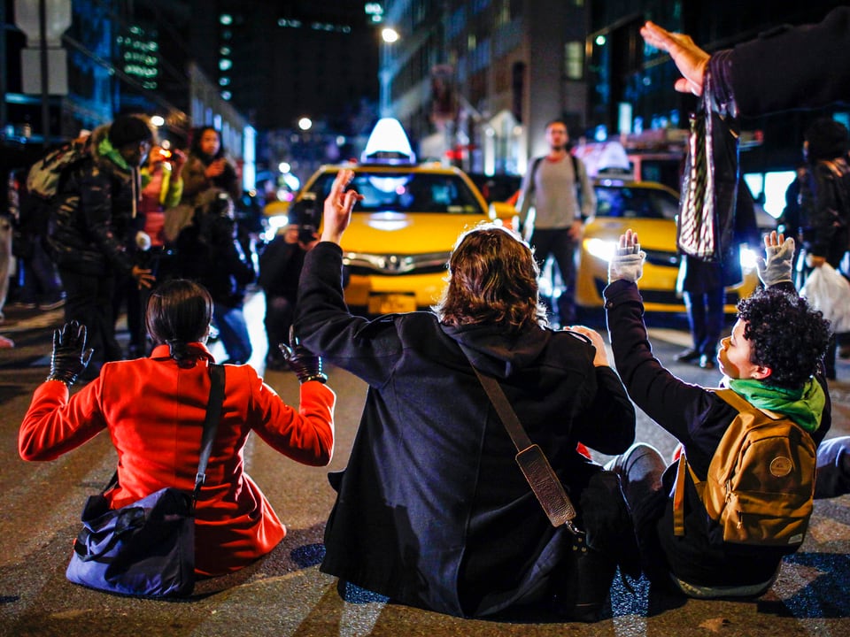 Sitzende Demonstranten, im Hintergrund sind gelbe Taxis erkennbar.