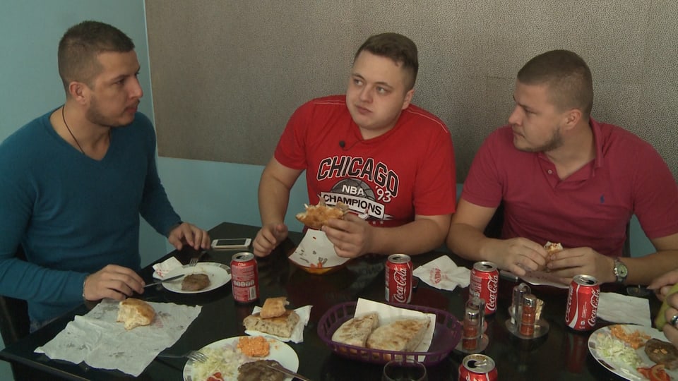 Drei junge Männer sitzen am Tisch. Sie essen und trinken. 
