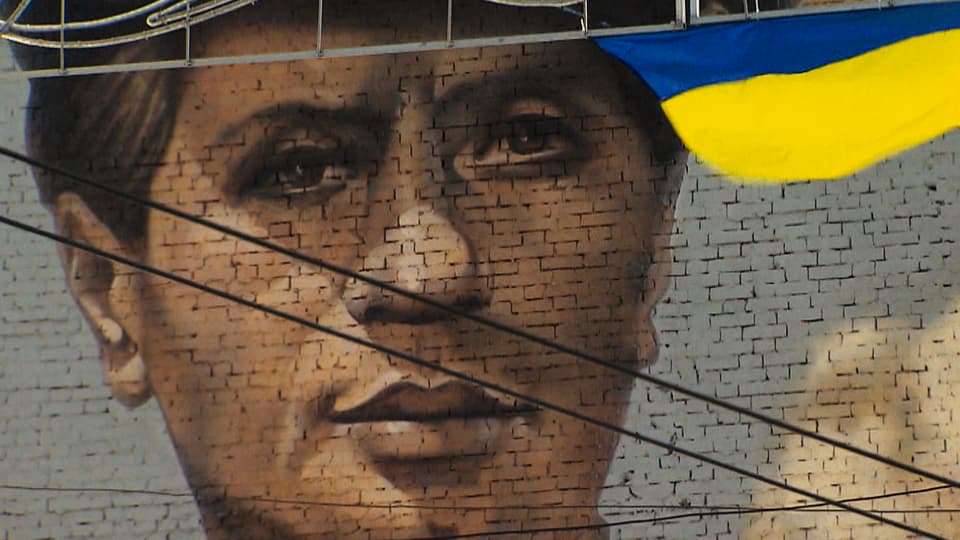 Auf einer Hauswand hat jemand eine ukrainische Flagge und ein Gesicht gemalt.