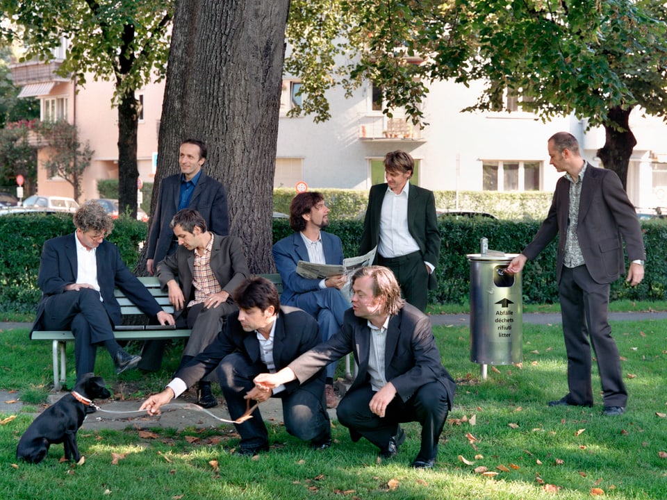 Acht Männer in Anzügen in einem Park.